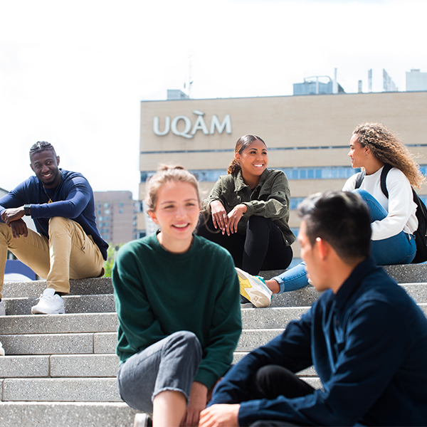 Groupe d'étudiant assis sur un escalier avec un bâtiment de l'UQAM en arrière plan